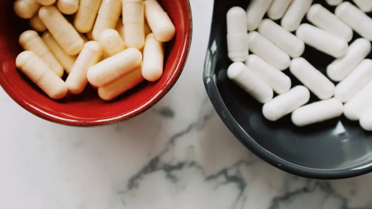 A dog's food bowl on a kitchen floor with a probiotic capsule set beside it