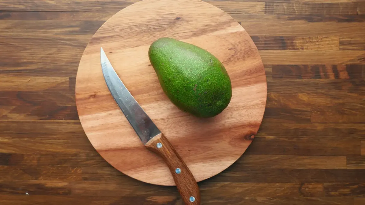 A halved avocado on a cutting board with a dog sniffing nearby