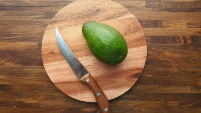 A halved avocado on a cutting board with a dog sniffing nearby