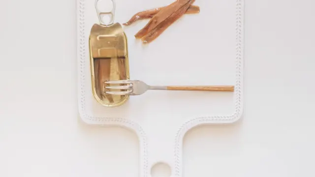 Canned sardines and a bottle of fish oil capsules on a wooden counter