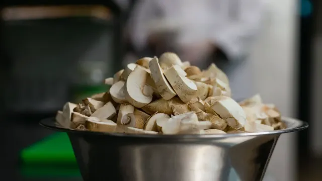 Sliced button mushrooms on a wooden cutting board beside a stainless dog bowl