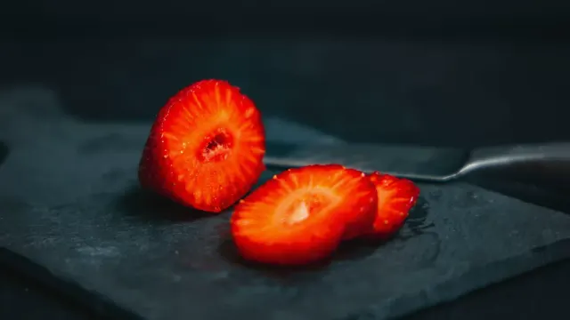 Sliced fresh strawberries on a wooden cutting board next to a small dog