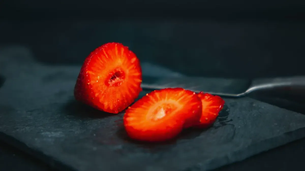 Sliced fresh strawberries on a wooden cutting board next to a small dog